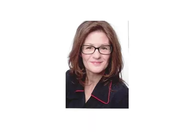 A woman with brown hair and glasses smiles at the camera. She is wearing a black top with red accents.