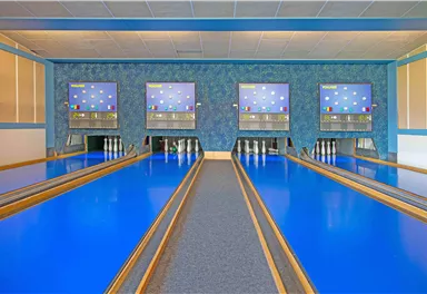 Eine Bowlingbahn mit leuchtenblauen Bahnen und digitalen Anzeigetafeln. Der Raum ist hell und modern gestaltet.