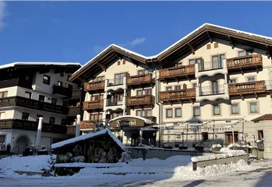 Ein gemütliches Hotel in den Bergen, umgeben von Schnee. Der klare Himmel und die alpine Architektur schaffen eine einladende Atmosphäre.