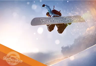A snowboarder jumps through the air at high speed. In the background, snow and a blue sky can be seen.