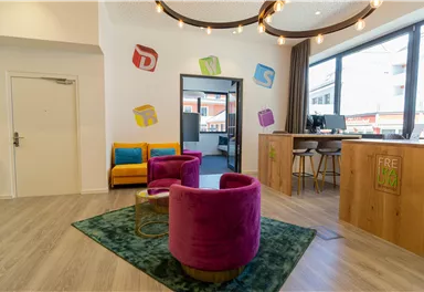 A modern reception area with colorful furniture and a friendly atmosphere. The seating area consists of purple armchairs and a wooden counter.