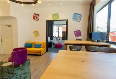 A modern office with colorful wall decorations and cozy seating. The space is bright and inviting, ideal for creative work.