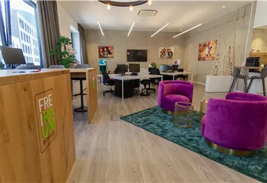A modern office with bright colors and stylish furniture. In the foreground, there are two purple armchairs on a carpet.