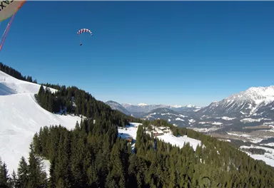 Ein klarer blauer Himmel über einer wunderschönen Berglandschaft mit schneebedeckten Hängen. Im Hintergrund sind beeindruckende Berge und dichte Wälder zu sehen.