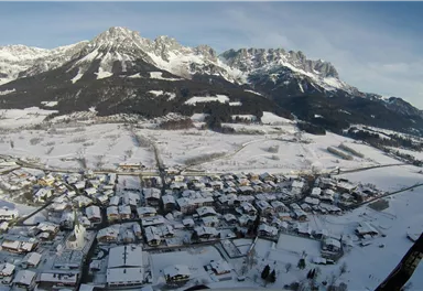 Eine schneebedeckte Landschaft mit einem kleinen Dorf und beeindruckenden Bergen im Hintergrund. Die ruhige Winteratmosphäre strahlt Frieden aus.