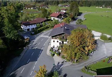 Eine malerische Dorfansicht mit traditionellen Häusern und einer ruhigen Straße. Die Umgebung ist grün und von Bäumen umgeben.