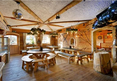 A cozy restaurant with wooden tables and benches. The rooms are decorated in a rustic style and are well lit.