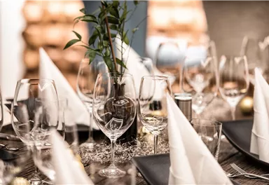 A festively laid table with elegant glasses and folded napkins. In the center, there is a small plant as a decoration.