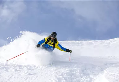A skier is skiing through the fresh snow. The sky is clear and blue.