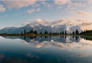 An impressive landscape with high mountains and gentle clouds. A quiet lake reflects the mountains and the sky.