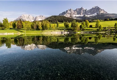 A picturesque landscape with a tranquil lake and gentle hills. In the background, majestic mountains rise under a clear sky.