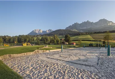 Ein Spielplatz mit Sandkasten und Blick auf die Berge. Die Umgebung ist grün und sonnig.