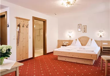 A bright room with two beds and a red carpet. There are wood details and a small table with a flower.