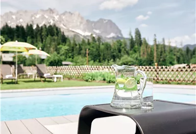 A beautiful pool with a view of the mountains. A carafe of water and lemons is on a table.