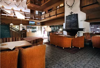 A cozy lobby with wooden elements and comfortable orange seating. In the background, large windows and a pleasant, inviting atmosphere can be seen.