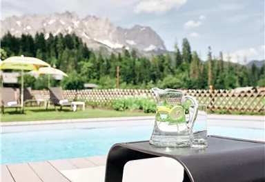 A beautiful pool with a view of the mountains. A carafe of water and lemons is on a table.