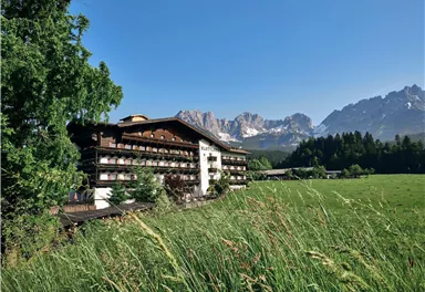 A picturesque hotel amidst green meadows and majestic mountains. The clear sky and peaceful surroundings invite you to relax.