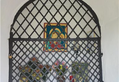 An adorned niche with a lattice, featuring a colorful picture and a floral arrangement. The niche appears peaceful and inviting.