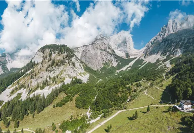 Eine beeindruckende Berglandschaft mit grünen Wiesen und hohen Gipfeln. Der Himmel ist teilweise bewölkt, was die natürliche Schönheit verstärkt.