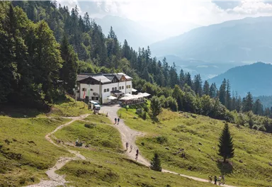 Ein malerisches Berghaus umgeben von grünen Wiesen und Bäumen. Der Weg führt zu dem Gebäude, das einen atemberaubenden Ausblick auf die Landschaft bietet.