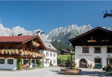 A picturesque alpine landscape with traditional wooden houses. In the background, majestic mountains rise under a clear blue sky.