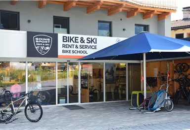 A shop for bike and ski rentals with a large glass front. In front of the entrance are several bicycles and a cart.