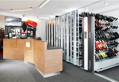 Ein moderner Verkaufsraum mit einem Empfangstresen und Schuhregalen. Auf der rechten Seite befinden sich verschiedene Schuhpaare in verschiedenen Farben.