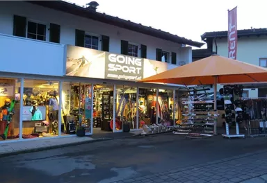 Ein Sportgeschäft mit bunten Sportartikeln und Ausrüstung. Es gibt einen großen orangen Sonnenschirm vor dem Laden.