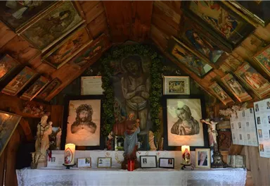 A small room with religious images and statues. On the table, candles and photos are arranged.