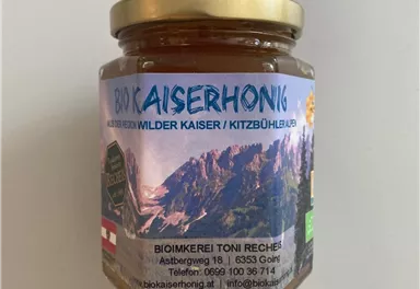 A jar of organic Kaiser honey with a golden lid. The label features the mountains of the Wild Kaiser and information about the beekeeping.