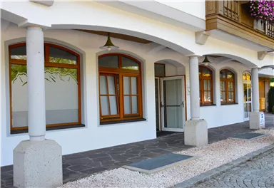 Ein Haus mit einem eleganten Eingang und mehreren Fenstern. Die Fassade ist hell gestrichen, und der Boden ist mit Kieselsteinen gestaltet.