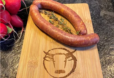 A wooden board with the inscription "Kaiser Wagyu" displays two sausages and fresh radishes. The sausages are on a kitchen table and look appetizing.