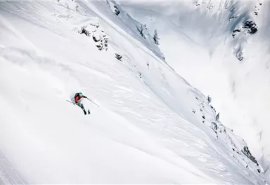A skier is traveling down a snow-covered slope in the mountains. The scenery is impressive and the surroundings appear untouched.