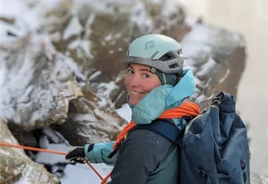 A person climbing in snow-covered terrain. They are wearing a helmet and backpack and are holding ropes in their hands.