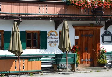 Ein traditionelles Restaurant mit einer einladenden Eingangstür und blühenden Pflanzen. Die grünen Fensterläden und Sonnenschirme verleihen dem Ort einen gemütlichen Charme.