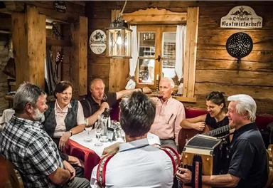 Eine gesellige Runde von Menschen in einem rustikalen Restaurant. Sie unterhalten sich, singen und spielen traditionelle Musik.