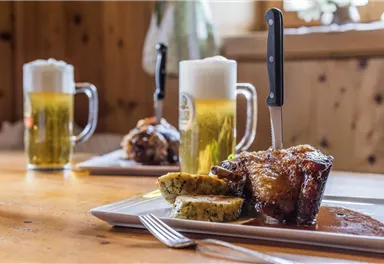 Ein köstliches Gericht mit Fleisch und Beilagen auf einem Teller. Im Hintergrund stehen zwei Gläser Bier.