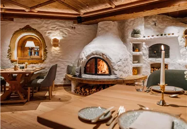 Ein gemütliches Restaurant mit einem offenen Kamin und rustikalem Holzdekor. Die Tische sind elegant gedeckt und schaffen eine einladende Atmosphäre.