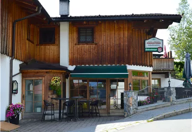 A cozy inn with a wooden facade and a terrace. Surrounded by flowers and an inviting ambiance.