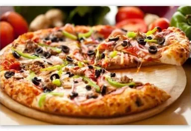 A delicious pizza with cheese, meat, olives, and bell peppers. Fresh vegetable ingredients can be seen in the background.