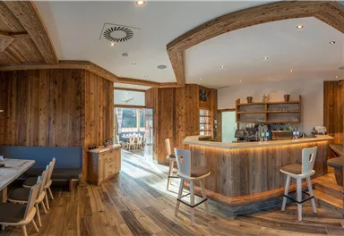 Ein modernes Restaurant mit Holzelementen und gemütlicher Atmosphäre. Die Bar ist gut ausgestattet, und es gibt einen Blick ins Freie.