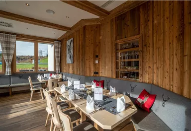 Ein gemütliches Restaurant mit Holzwänden und einem großen Fenster. Die Tische sind festlich gedeckt und es gibt bequeme Sitzgelegenheiten.