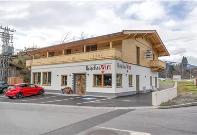 A modern building in alpine style is located at a street corner. A red car is parked in front of the house.
