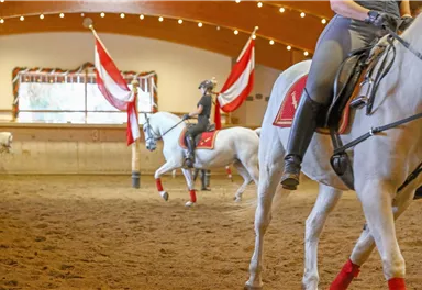 A riding arena with several horses and riders. The atmosphere is festive with red and white flags.