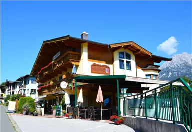 Ein charmantes Gebäude im alpinen Stil mit Balkonen und bunten Blumen. Die Umgebung ist sauber und freundlich, mit Blick auf die Berge.