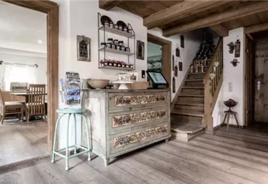 A cozy entryway with a decorative sideboard and a staircase in the background. The room is bright and inviting, with wooden floors and a rustic flair.