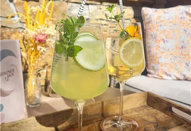 Two glasses with refreshing cocktails are placed on a wooden tray. The drinks are garnished with lime slices and fresh mint.