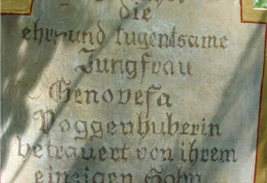 Ein Schild mit der Inschrift über die ehrwürdige Jungfrau Genoveva, das in einem Garten angebracht ist. Es ist Teil eines historischen Ortes in der Nähe von Kitzbühel.