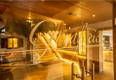 An inviting entrance area with a stylish glass door. In the background, a staircase and warm light are visible.