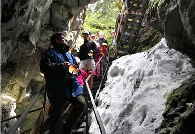 A group of people is climbing a staircase in a cave. Rocks and snow are visible around them.